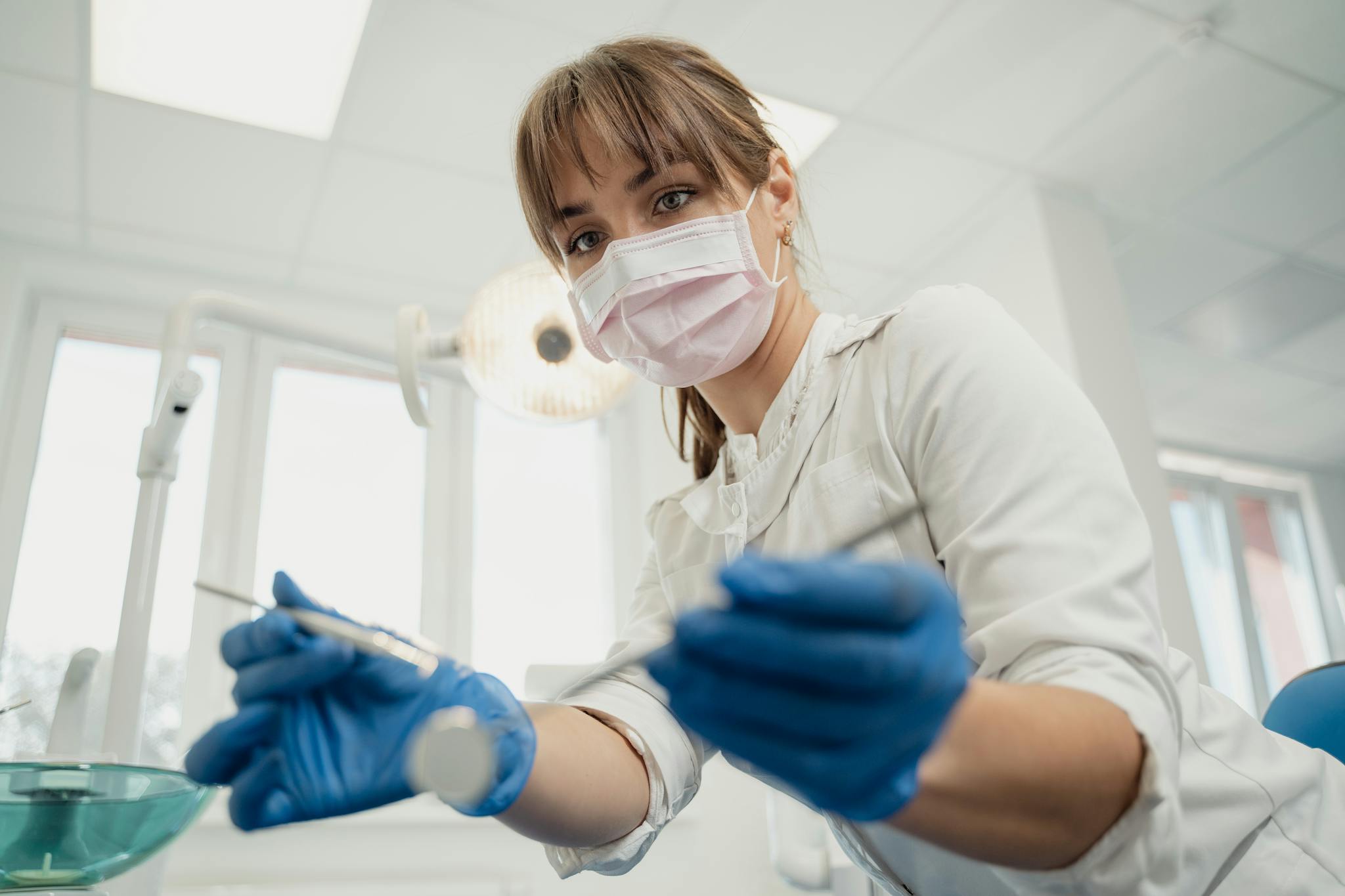 A female dentist wearing gloves and a mask preparing for a dental procedure in a clinic.